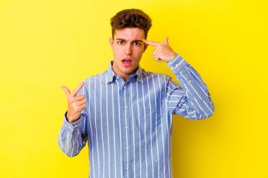 Sarı arka planda izole edilmiş genç beyaz adam işaret parmağıyla hayal kırıklığı jesti yapıyor..