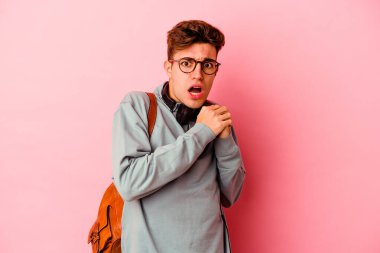 Genç bir öğrenci pembe arka planda izole edilmiş korkmuş ve korkmuş..