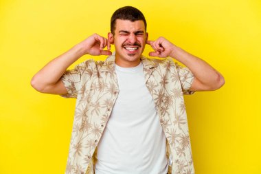 Sarı arka planda izole edilmiş, elleri kulaklarında genç, beyaz bir adam..