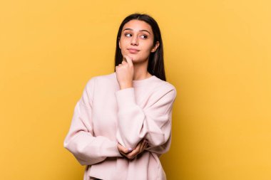 Genç Hintli kadın sarı arka planda izole edilmiş düşünüyor ve yukarı bakıyor, yansıtıyor, düşünüyor, hayal kuruyor..