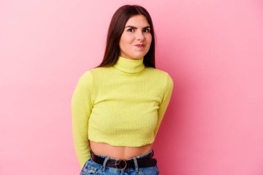 Pembe arka planda soyutlanmış beyaz bir kadın omuzlarını silkeliyor ve gözleri açık..