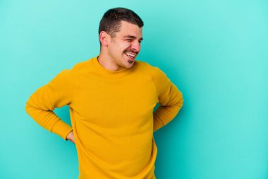 Mavi arka planda izole edilmiş genç beyaz adam gülüyor ve gözlerini kapıyor, rahatlamış ve mutlu hissediyor..