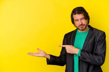 Sarı arka planda izole edilmiş orta yaşlı beyaz bir adam, elinde palmiye ağacının bir kopyasını tutarken heyecanlı..