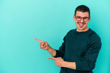 Mavi arka planda izole edilmiş genç beyaz adam işaret parmağıyla fotokopi alanını işaret ederek heyecan ve arzusunu ifade ediyor..