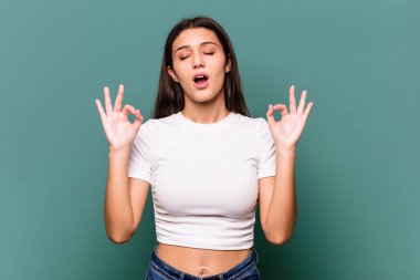 Mavi arka planda izole edilmiş genç Hintli kadın yoğun bir günün ardından rahatlıyor, yoga yapıyor..