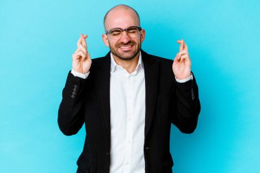 Genç beyaz tenli kel adam, şans dilemek için mavi arka planda izole edildi.