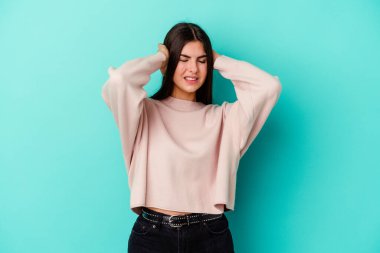 Mavi arka planda izole edilmiş genç beyaz kadın kulaklarını elleriyle kapatıyor..