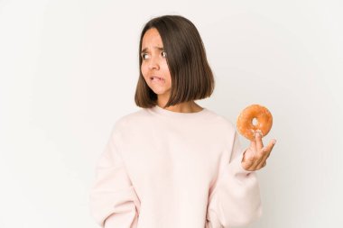 Genç İspanyol kadın donut yiyor, kafası karışık, şüpheci ve kararsız..