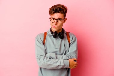 Pembe arka planda izole edilmiş genç bir öğrenci hoşnutsuzca kaşlarını çatmış, kollarını kavuşturmuş..