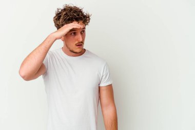 Beyaz arka planda izole edilmiş genç beyaz bir adam uzaklara bakıyor ve elini alnına koyuyor..