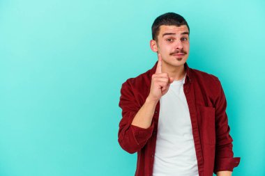 Mavi arka planda izole edilmiş genç beyaz adam bir numarayı parmağıyla gösteriyor..