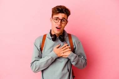 Pembe arka planda izole edilmiş genç bir öğrencinin dostane bir ifadesi var. Avuçlarını göğsüne bastırıyor. Aşk konsepti.