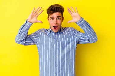 Sarı arka planda izole edilmiş genç beyaz bir adam zaferi ya da başarıyı kutluyor, şaşırıyor ve şok oluyor..