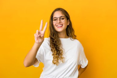 Genç beyaz kadın zafer işareti gösteriyor ve gülümsüyor..