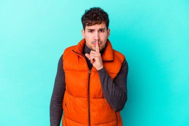 Mavi arka planda izole edilmiş genç beyaz bir adam ya sır saklıyor ya da sessizlik istiyor..