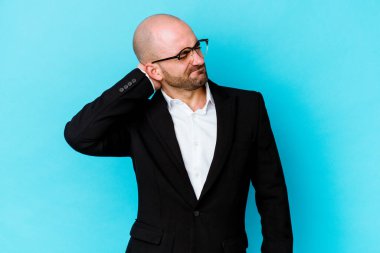 Genç, beyaz, kel bir adam mavi arka planda izole edilmiş. Stres yüzünden boynu ağrıyor, masaj yapıyor ve elle dokunuyor..