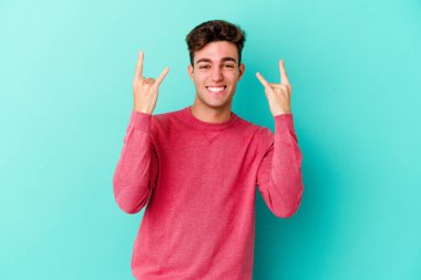 Mavi arka planda izole edilmiş genç beyaz adam boynuzlarını devrim konsepti olarak gösteriyor..