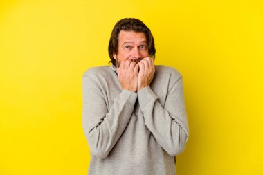 Orta yaşlı beyaz bir adam sarı arka planda izole edilmiş tırnak yiyor, gergin ve çok endişeli..