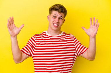 Sarı arka planda izole edilmiş genç beyaz bir adam zaferi ya da başarıyı kutluyor, şaşırıyor ve şok oluyor..