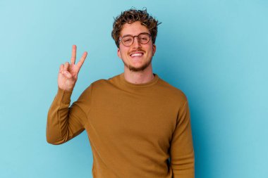 Mavi arka planda gözlüklü genç beyaz adam zafer işareti gösteriyor ve gülümsüyor..