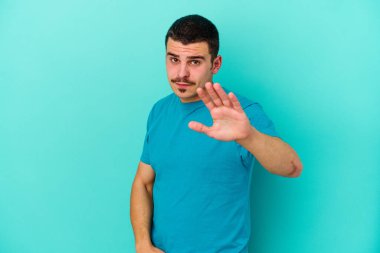 Mavi arka planda izole genç beyaz adam yakın bir tehlike nedeniyle şoka uğruyor