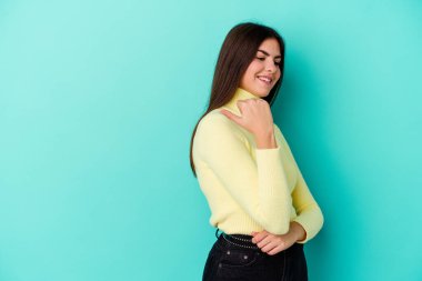 Kafkasyalı genç bir kadın mavi arka planda izole edilmiş başparmak uzakta, gülüyor ve kaygısız.