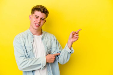 Sarı arka planda izole edilmiş genç beyaz adam işaret parmağıyla işaret ederek gülümsüyor..