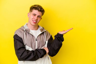 Sarı arka planda izole edilmiş genç beyaz bir adam bir palmiye üzerinde fotokopi alanı gösteriyor ve belinde başka bir el tutuyor..