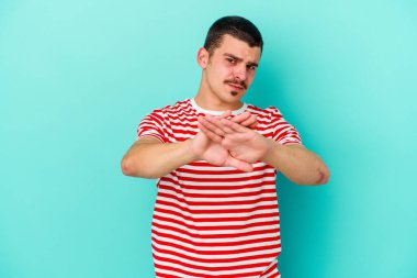 Kafkasyalı genç adam mavi arka planda izole edilmiş bir şekilde inkar hareketi yapıyor.