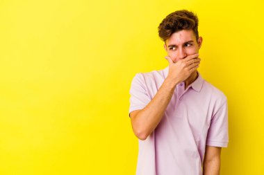 Kafkasyalı genç adam sarı arka planda izole edilmiş. Düşünceli bir şekilde, ağzını eliyle kapatan bir fotokopi odasına bakıyor..