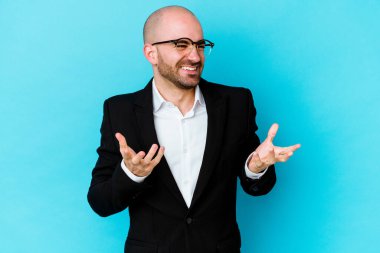Genç, beyaz, kel bir adam mavi arka planda izole edilmiş neşeli bir şekilde gülüyor. Mutluluk kavramı.