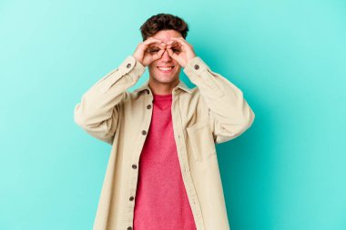 Mavi arka planda izole edilmiş genç beyaz adam gözlerinde sorun olmadığını gösteriyor.