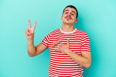 Kafkasyalı genç adam mavi arka planda izole edilmiş yemin ediyor, elini göğsüne koyuyor..