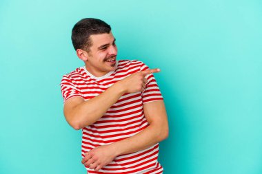 Mavi arka planda soyutlanmış genç beyaz bir adam gülümsüyor, neşeli ve keyifli görünüyor..