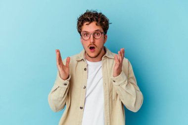 Mavi arka planda gözlük takan genç beyaz adam şaşırdı ve şok oldu..