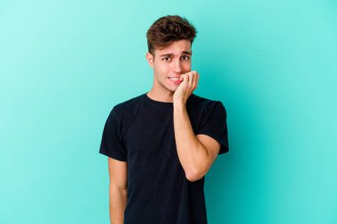 Mavi arka planda izole edilmiş, tırnak yiyen, gergin ve endişeli genç bir beyaz adam..