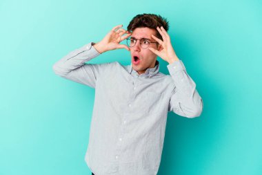 Mavi arka planda izole edilmiş genç beyaz adam bir başarı fırsatı bulmak için gözlerini açık tutuyor..