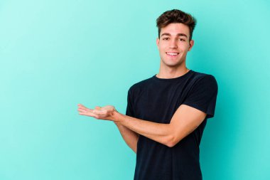 Mavi arka planda izole edilmiş genç beyaz bir adam palmiyesinde bir kopya alanı tutuyor..