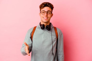 Pembe arka planda izole edilmiş genç bir öğrenci selamlama jesti olarak kameraya elini uzatıyor..