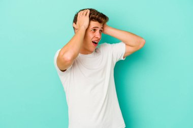 Genç beyaz adam mavi arka planda izole edilmiş bağırıyor, çok heyecanlı, tutkulu, bir şeyden memnun..