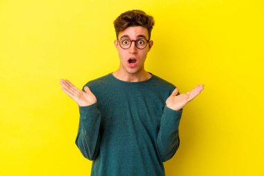 Sarı arka planda izole edilmiş genç beyaz adam şaşırdı ve şok oldu..