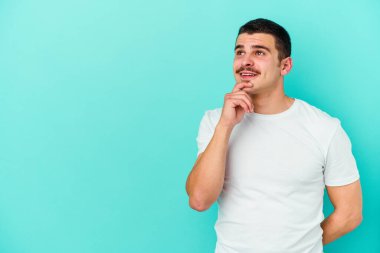 Mavi arka planda izole edilmiş genç beyaz adam rahatlamış bir şeyin fotokopi odasına baktığını düşünüyor..