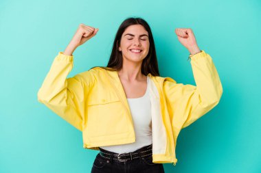 Mavi arka planda izole edilmiş genç beyaz kadın zaferi, tutkuyu ve coşkuyu kutluyor, mutlu bir ifade..