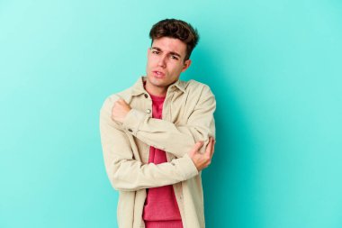 Kafkasyalı genç adam mavi arka planda izole edilmiş dirsek masajı yapıyor, kötü bir hareketin ardından acı çekiyor..