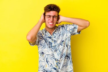 Sarı arka planda izole edilmiş genç beyaz adam elleriyle kulakları örtüyor..