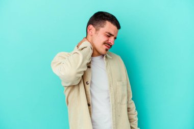 Kafkasyalı genç adam mavi arka planda izole edilmiş. Stres yüzünden boynu ağrıyor. Masaj yapıyor ve elle dokunuyor..