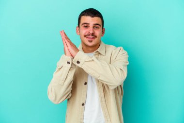 Kafkasyalı genç adam mavi arka planda izole edilmiş enerjik ve rahat hissediyor, ellerini ovuşturuyor kendinden emin.