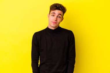Sarı arka planda izole edilmiş genç beyaz adam omuzlarını silkeliyor ve gözleri açık..