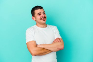 Kafkasyalı genç adam mavi arka planda izole edilmiş hedeflerine ve amaçlarına ulaşma hayali kuruyor.