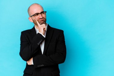 Kafkasyalı genç bir adam mavi arka planda izole edilmiş şüpheli ve şüpheci bir ifadeyle yana bakıyor..